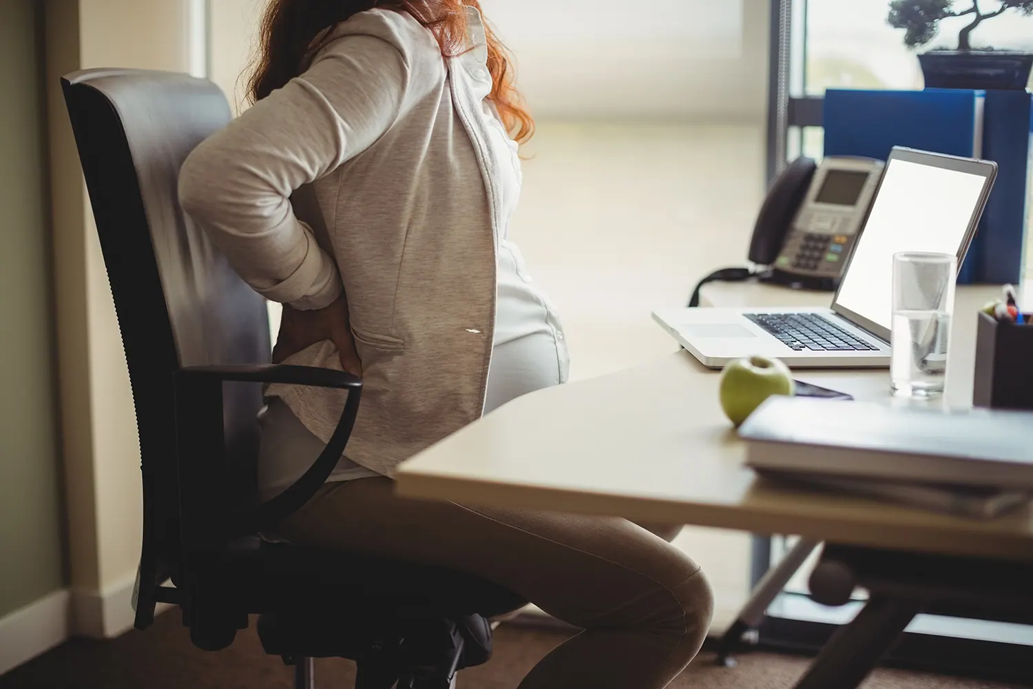 a woman suffering from back pain from pregnancy while working